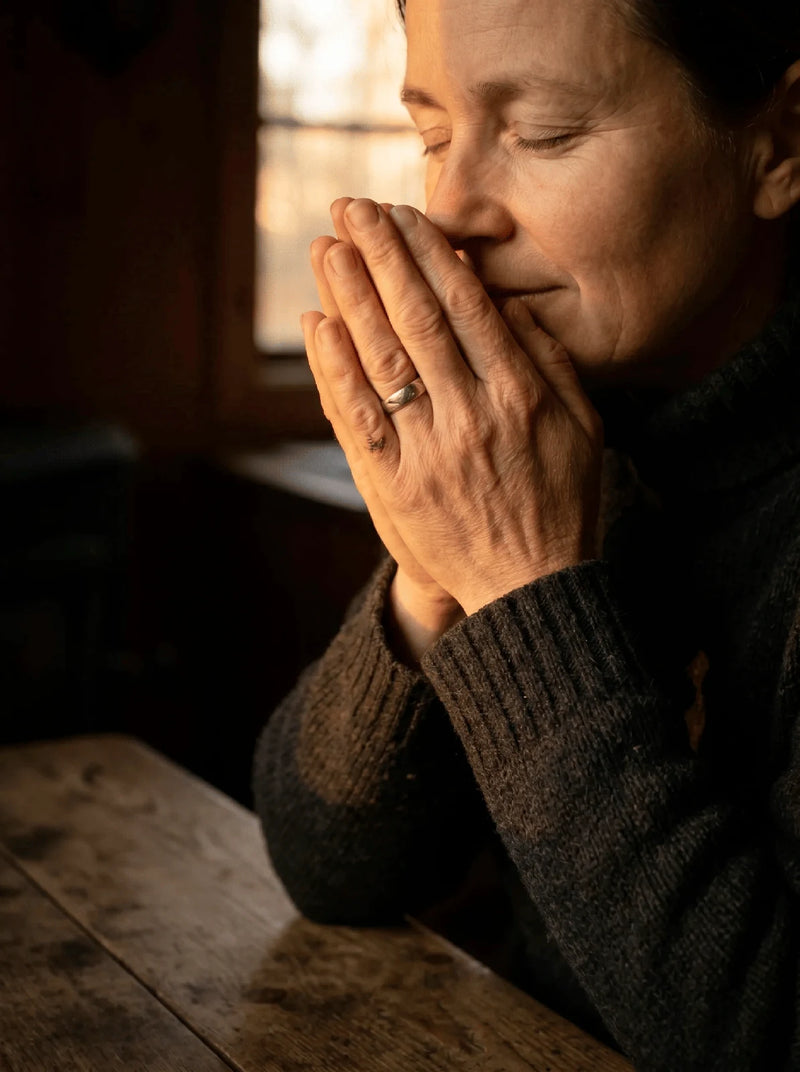 Een vrouw ademt diep vanuit haar samengevouwen handen bij haar gezicht, in warm, amberkleurig licht. Ritueel van de ademhaling.