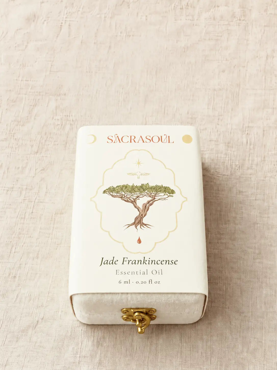 Pudełko w zadrukowanej białej obwolucie, na lnie. Na obwolucie widnieje SACRASOUL, potem drzewo kadzidłowe w złotym kartuszu, a pod nim Jade Frankincense, Essential Oil, 6 ml · 0.20 fl oz. Na otwartym końcu widać złote zapięcie.