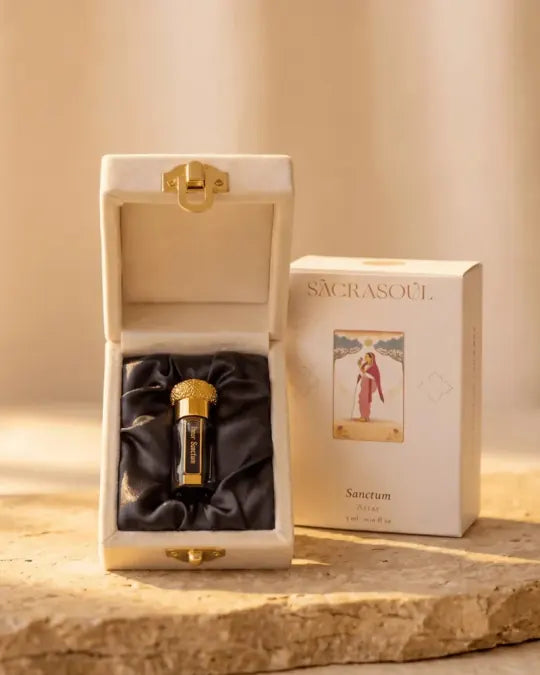 Het blauw-gouden Inner Sanctum-attarflesje op zwart satijn in het open crèmekleurige etui, naast het doosje met de tekst Sacrasoul, Sanctum Attar, 3 ml.